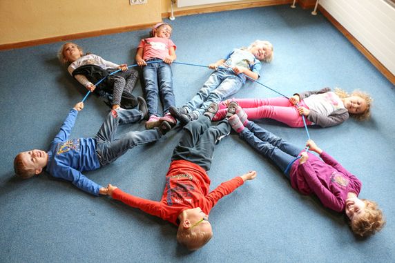 Kinder liegen im Kreis und halten ein Seil