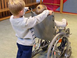 Kind schiebt ein anderes Kind im Rollstuhl